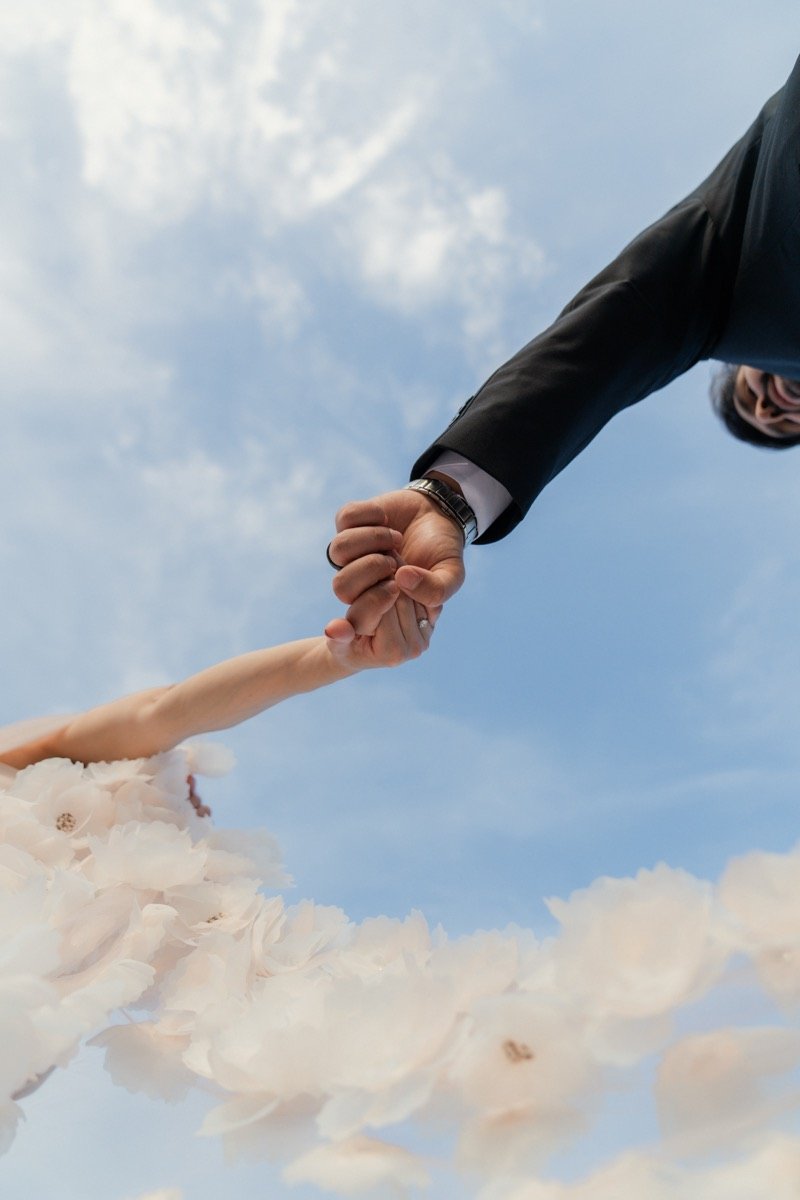 A hand reaching back for another against an open sky
